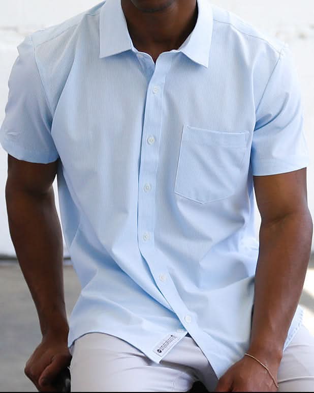 Man wearing a light blue shirt sitting against a white wall.
